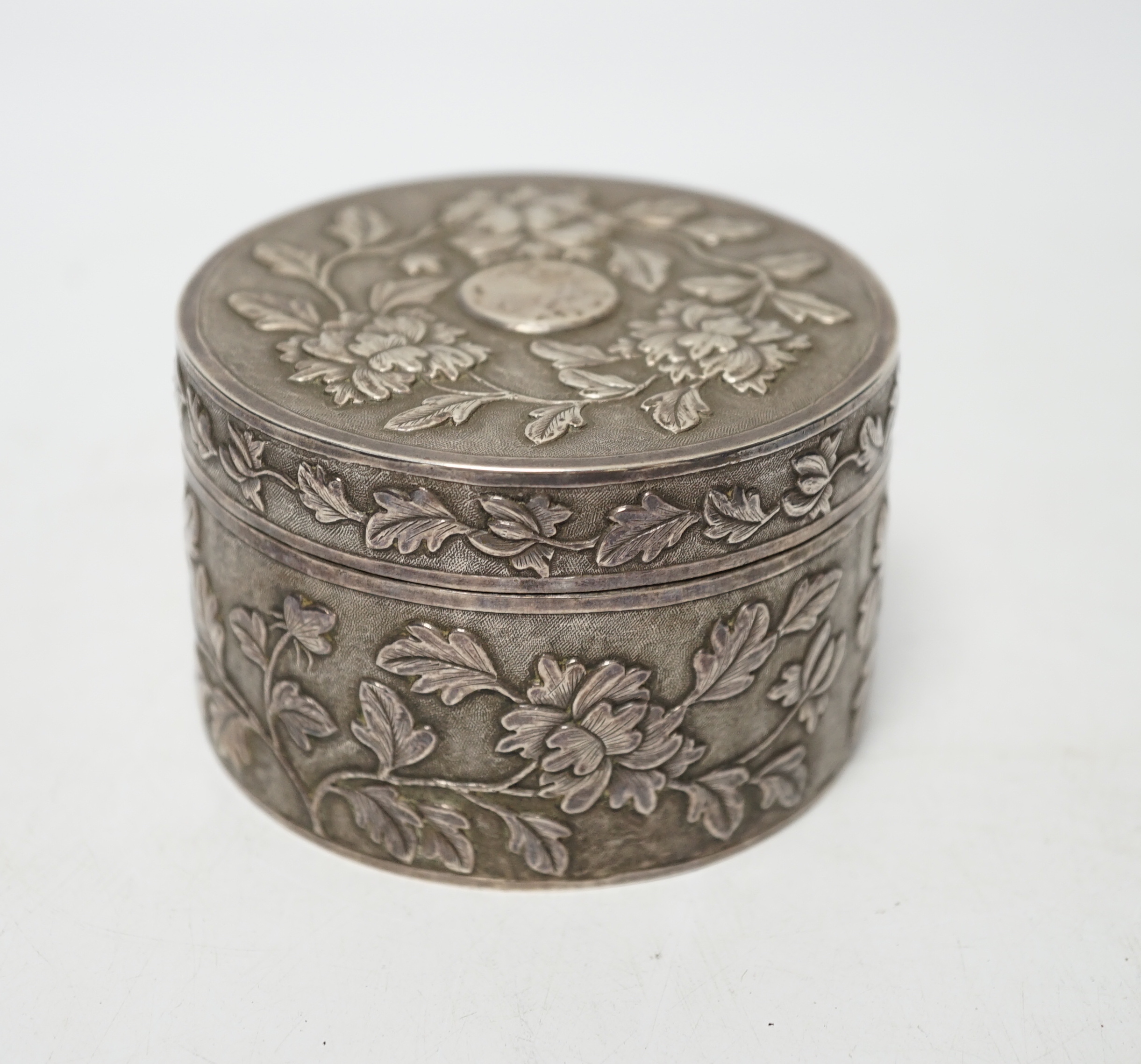 An early 20th century Chinese white metal circular box and cover, maker's mark MK, with foliate decoration and engraved inscription, diameter 82mm, 128 grams.